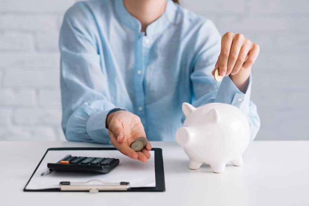 Senhora a organizar as suas finanças, colocando moedas no mealheiro e calculando as despesas e poupanças.